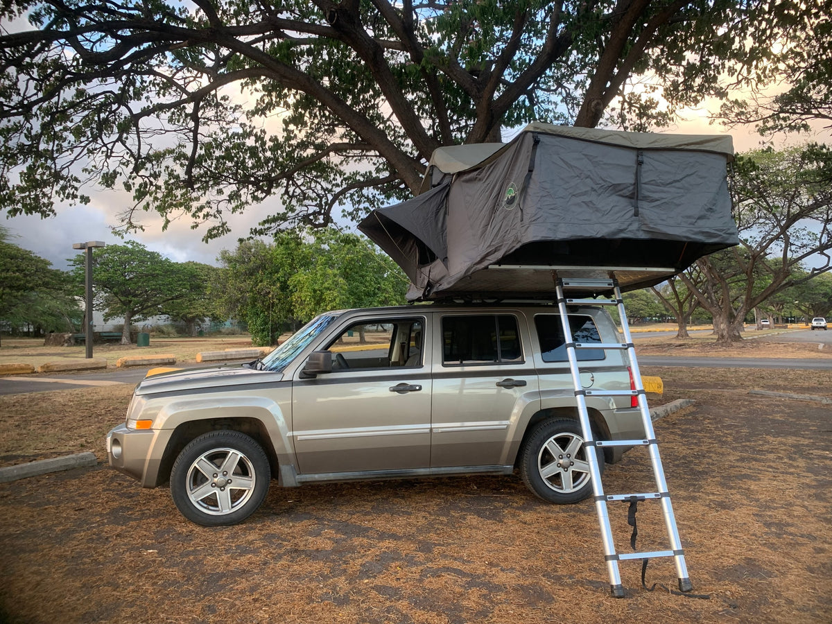 This Jeep Patriot SUV with a deployed rooftop tent offers a unique and compact camping experience, an alternative to RV rental. — photo 9