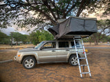 This Jeep Patriot SUV with a deployed rooftop tent offers a unique and compact camping experience, an alternative to RV rental.