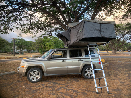 This Jeep Patriot SUV with a deployed rooftop tent offers a unique and compact camping experience, an alternative to RV rental.