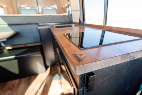 RV rental van's 46 NORTH LONG kitchen: sleek wooden countertop, induction cooktop & sink. Compact living on the go.