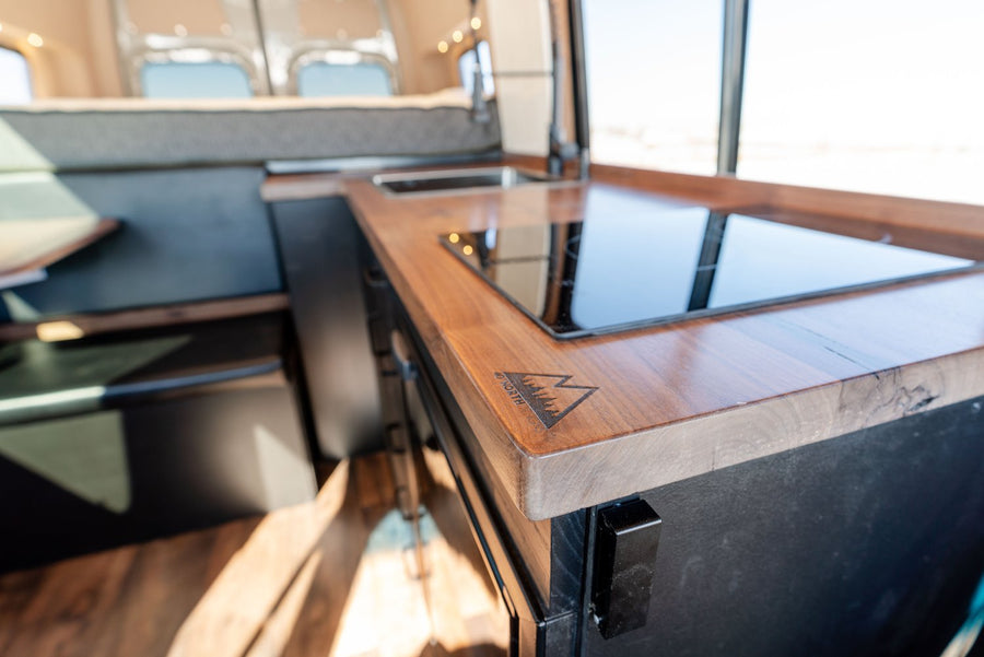 RV rental van's 46 NORTH LONG kitchen: sleek wooden countertop, induction cooktop & sink. Compact living on the go.