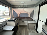 View inside a bright rv rental pop-up camper, showcasing a bed, compact kitchen, and seating area.