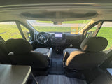 Inside an **rv rental**, looking forward past front seats to the dashboard, steering wheel, & windshield showing an outdoor field.
