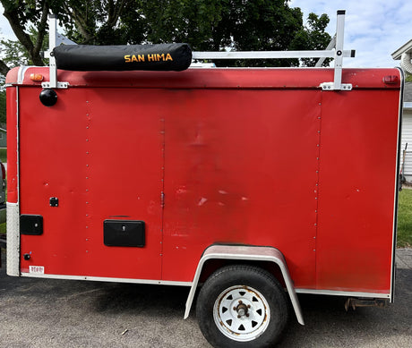 A red enclosed cargo trailer, equipped with a roof rack and shower hookup, perfect for an RV rental adventure.