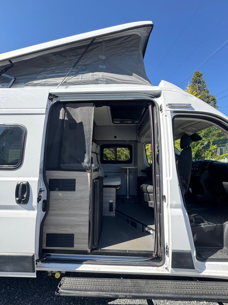 White RV rental with pop-top roof. Its side door is open, revealing a meticulously designed interior with kitchen, dining, and seating areas. — photo 3