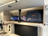 RV rental overhead storage with blankets and a 12V blanket, above a sink and window with blinds.