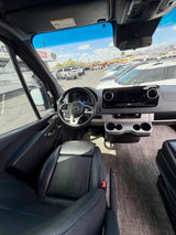 View from inside a modern Mercedes Sprinter van, likely an RV rental, showing the dashboard and a sunny parking lot.