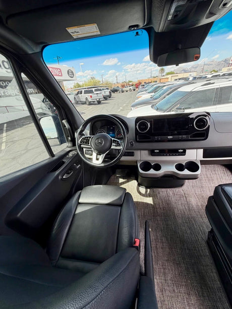 View from inside a modern Mercedes Sprinter van, likely an RV rental, showing the dashboard and a sunny parking lot.