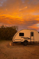 Enjoy a vibrant sunset with this cozy RV rental! A small travel trailer is parked, ready for your next nature adventure.