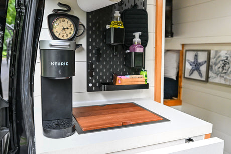 Modern RV rental kitchen with Keurig coffee machine, pegboard storage, and integrated cutting board on counter.