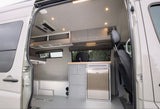 rv rental camper van interior. Features kitchenette with fridge, overhead cabinets, bed, and bright lighting.