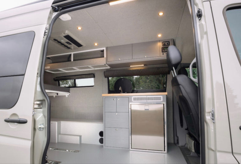 rv rental camper van interior. Features kitchenette with fridge, overhead cabinets, bed, and bright lighting. — photo 2