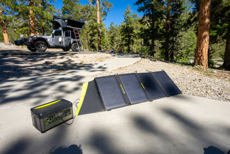 Off-grid RV rental setup: Goal Zero solar panel charges a Yeti power station next to a Jeep with a rooftop tent at a campsite.
