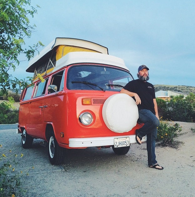 Bearded man leaning on a vintage orange VW camper van with a pop-top, ready for an RV rental road trip adventure!