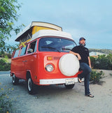 Bearded man leaning on a vintage orange VW camper van with a pop-top, ready for an RV rental road trip adventure!