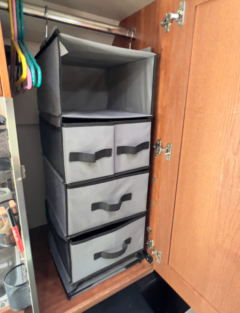 RV rental closet storage: A multi-tiered gray fabric organizer with pull-out drawers hangs from a rod in a wooden wardrobe.