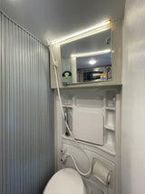 Inside an RV rental, a compact wet bath features a toilet, shower, and mirror, maximizing space for travel.