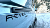 A light gray Winnebago Revel 4x4 camper van RV rental on a snowy road with mountains in the background.