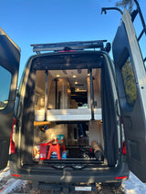 Back of an RV rental with doors open, revealing a modern interior, bed, and storage space.