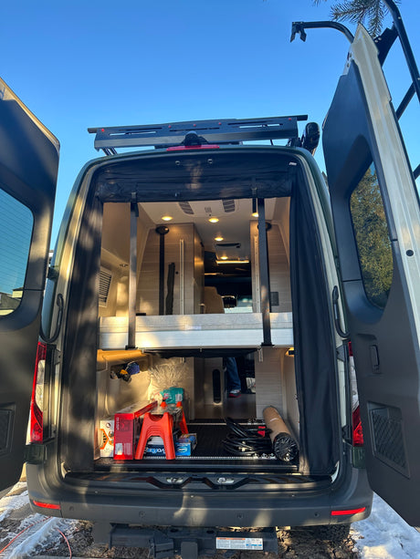Back of an RV rental with doors open, revealing a modern interior, bed, and storage space.