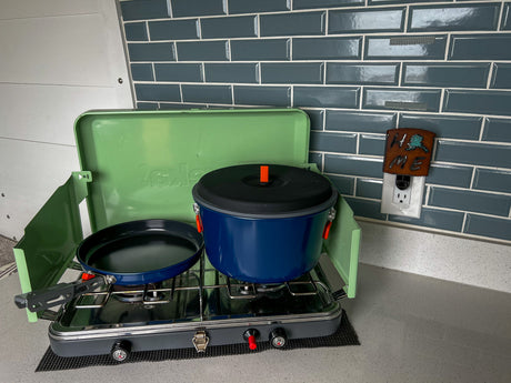 Compact RV rental kitchen: green portable camping stove with a blue pot & black pan on a gray counter.
