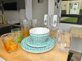 Inside an RV rental: new teal patterned dishes and assorted glassware on a wood counter, ready for travel.