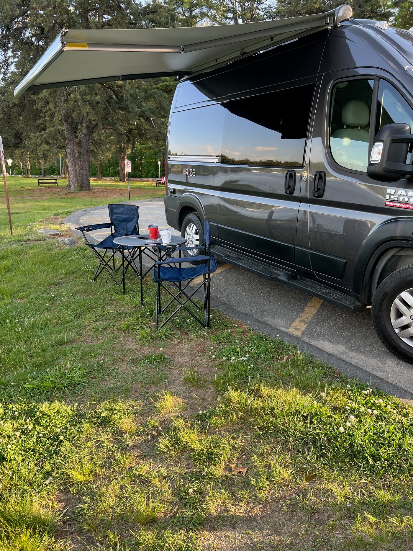 Grey RV rental van with extended awning, two blue chairs, and a table set up on the grass. — photo 6