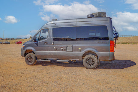 Rugged gray Mercedes Sprinter camper van, labeled "Tranquility," an ideal rv rental, parked on a gravel lot under a blue sky.