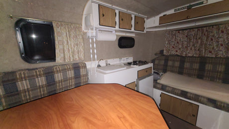 An rv rental's functional interior: kitchen, dining table, and plaid bench seating with a window view. Great for travel.