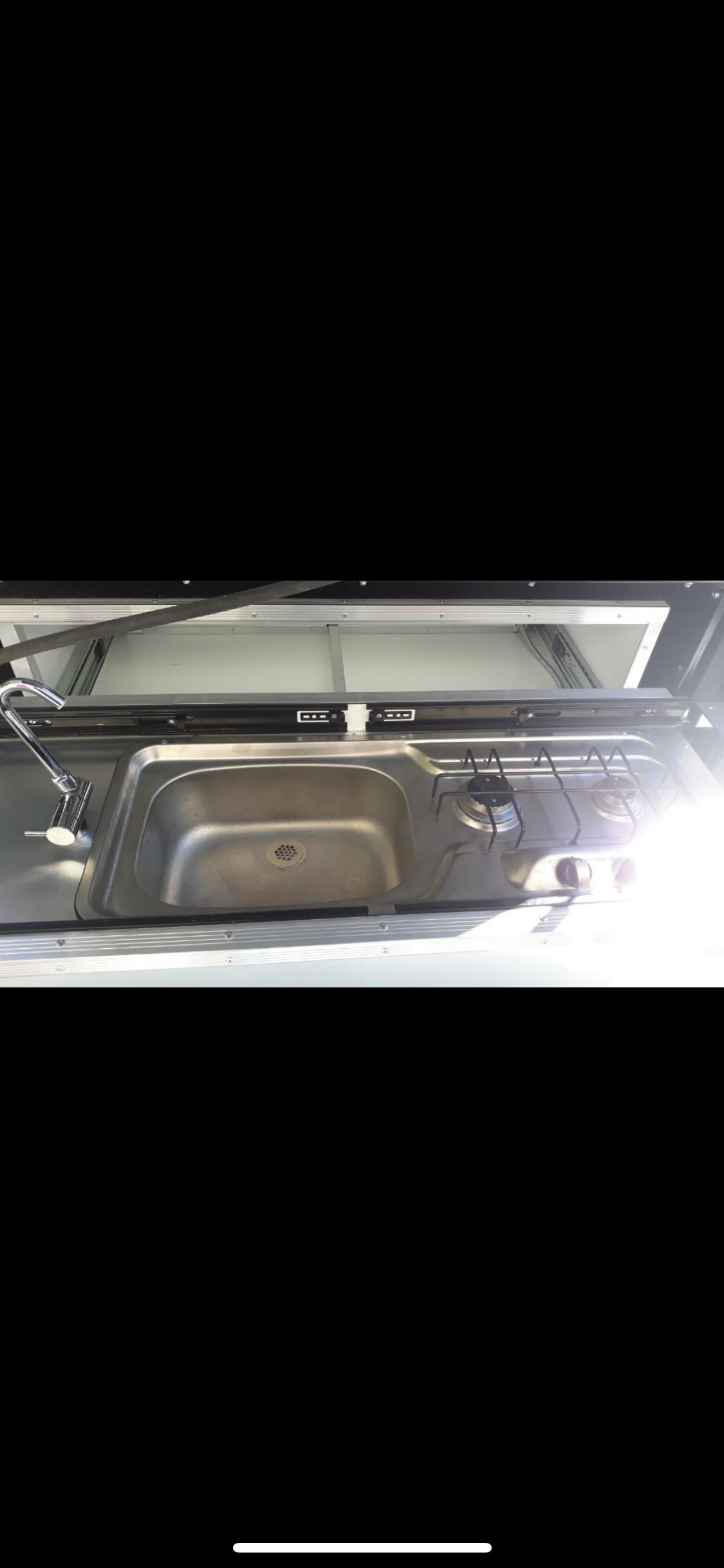 RV rental features a compact kitchen with a stainless steel sink and a two-burner stove.