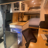 View inside an rv rental: functional kitchen, bunk beds, & workspace. Ideal for compact camper van adventures.