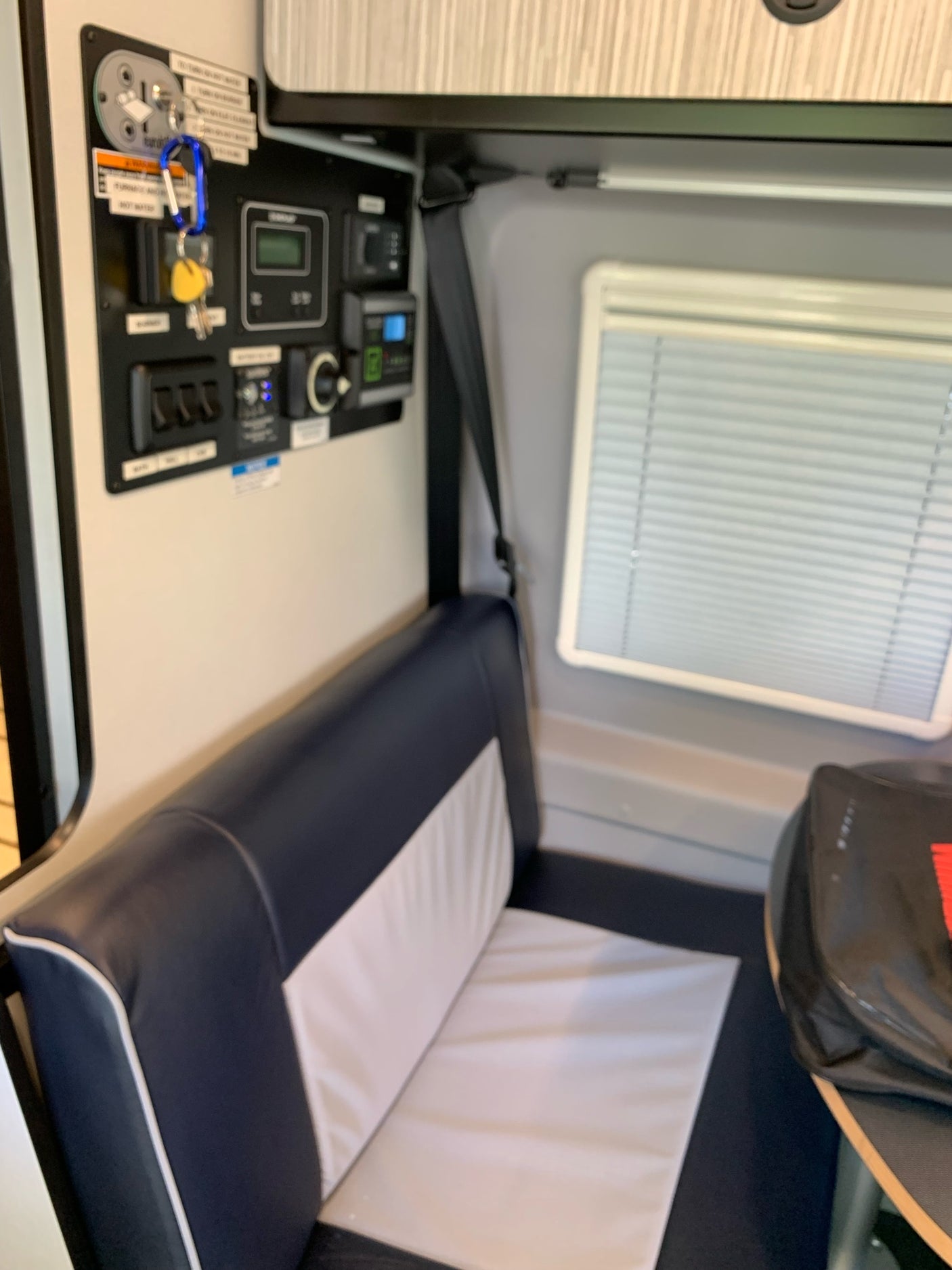 An RV rental interior shows a control panel with keys, a blue and white bench seat, and a window on the right wall.