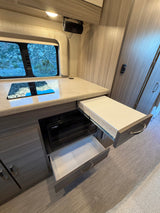 Modern rv rental galley featuring an induction cooktop, microwave, and open drawers. A JBL speaker is mounted overhead.