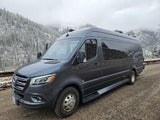Gray Mercedes-Benz Sprinter RV rental parked amidst snowy mountains and trees on a cloudy day.