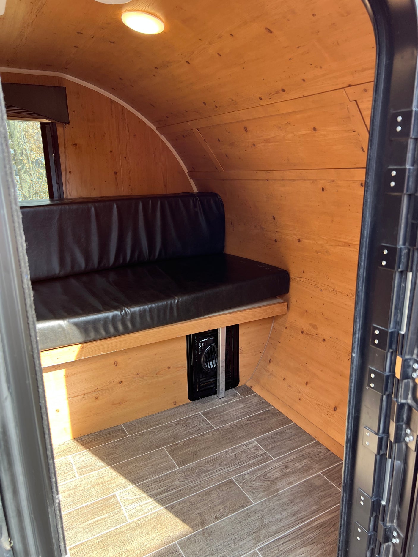 Inside an RV rental: Wooden walls & ceiling, black bench seat, and wood-look tile floor create a cozy camper space.