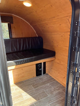 Inside an RV rental: Wooden walls & ceiling, black bench seat, and wood-look tile floor create a cozy camper space.