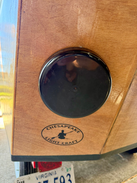 Wooden kayak/boat with round black hatch & Chesapeake Light Craft logo. Visible near a vehicle, possibly an RV rental trailer.