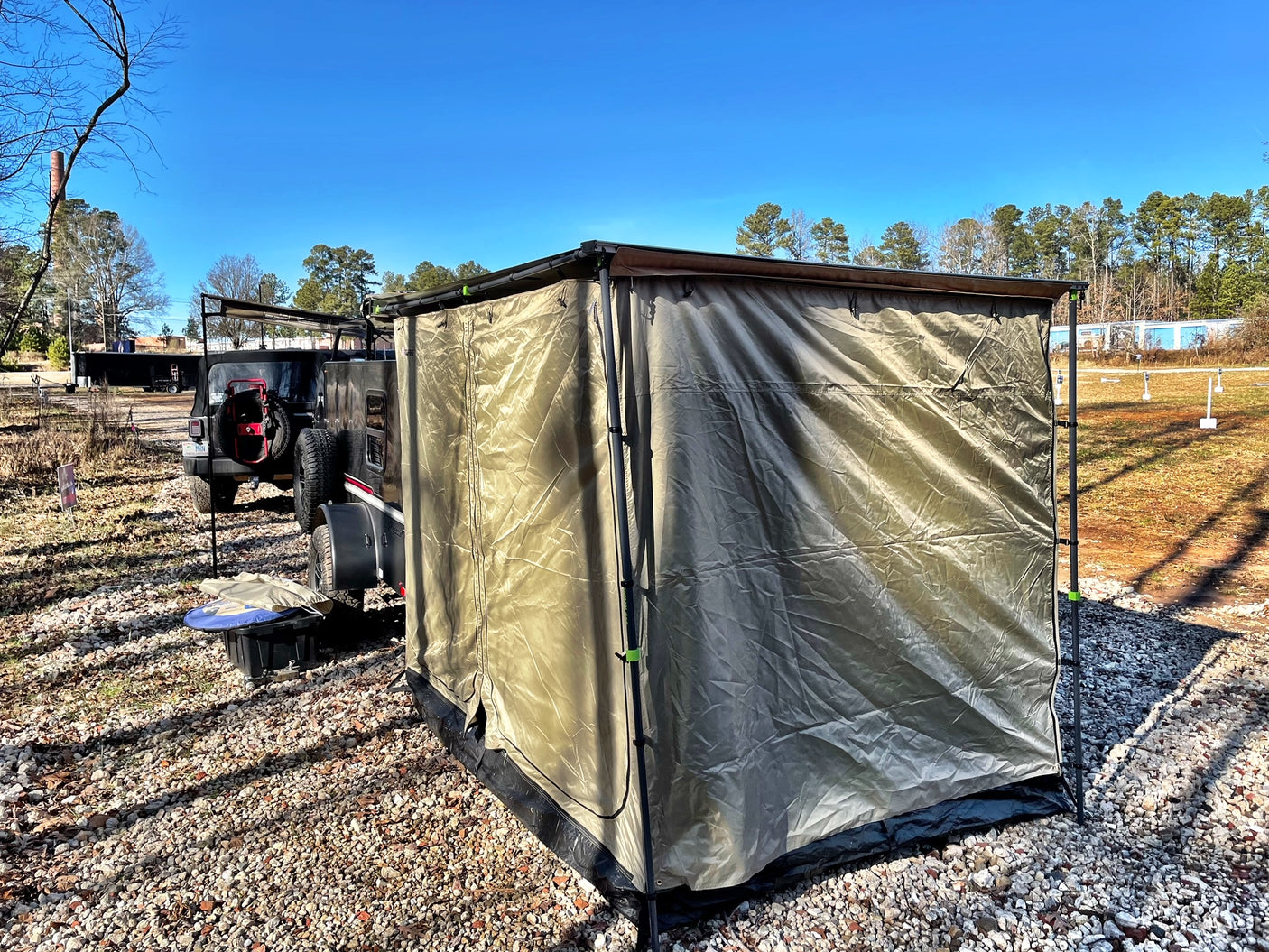 RV rental ready: Overland trailer with olive tent setup on gravel, offering spacious outdoor shelter for camping.