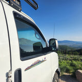 White rv rental camper van with a mountain decal overlooking a scenic vista under clear blue skies.