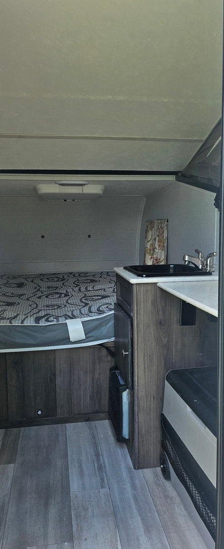 Inside a cozy rv rental: compact bedroom with patterned mattress, kitchenette with sink, wood-look cabinets, and flooring.