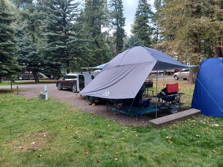 Campsite view: a grey awning extends from a compact travel trailer. This cozy setup is typical for an RV rental or personal RV.