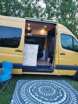 Custom yellow Sprinter camper van with open side door revealing a cozy, wood-paneled interior. Great for your rv rental.