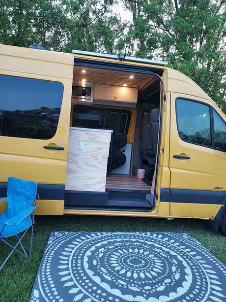 Custom yellow Sprinter camper van with open side door revealing a cozy, wood-paneled interior. Great for your rv rental.