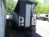Rear view of a Viking pop-up RV rental with an open door and steps, parked next to a building. Other RVs are in the background.