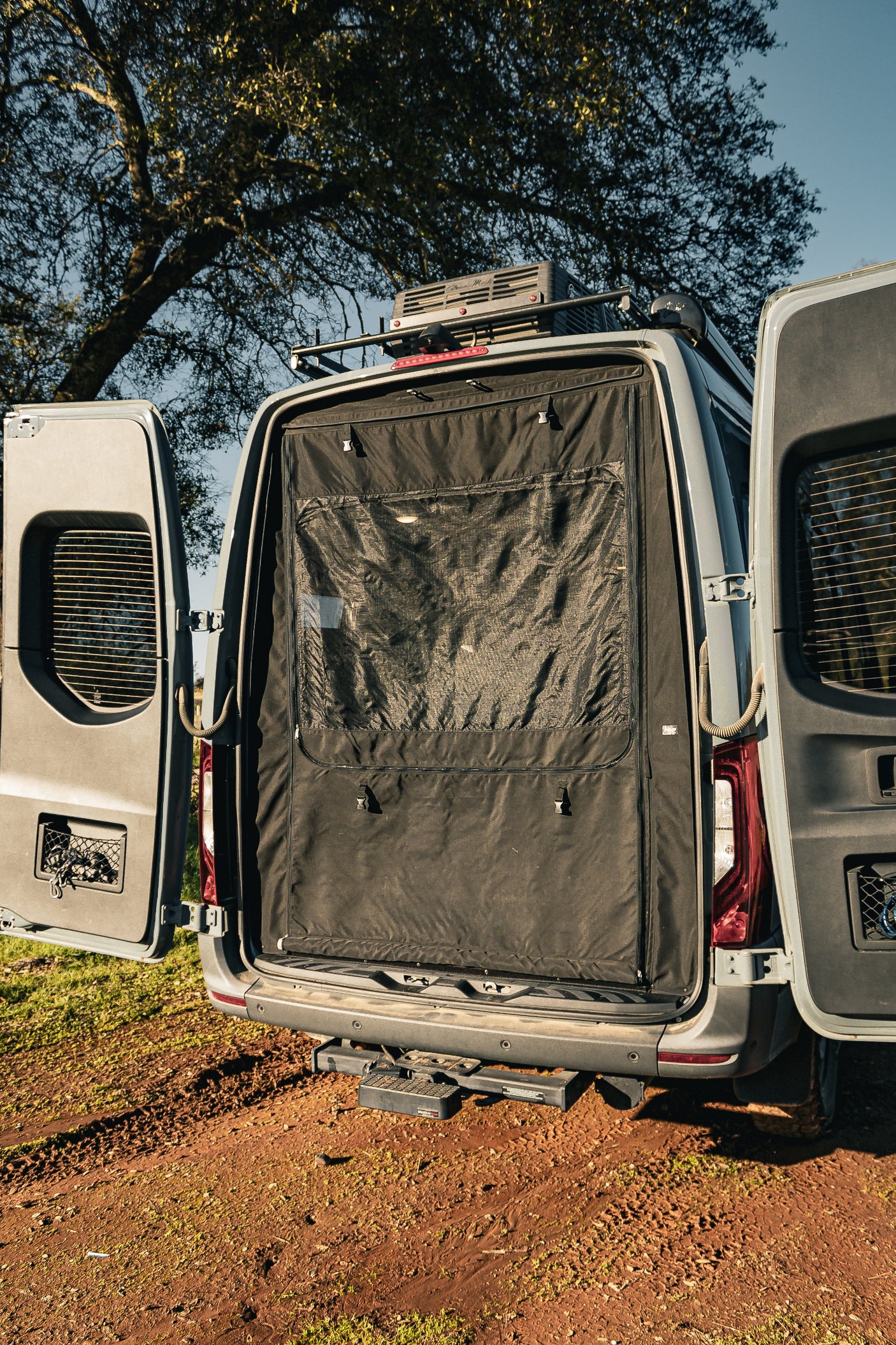Rear of an **RV rental** with open doors showcasing a black bug screen, roof cargo, and a robust setup for outdoor travel.