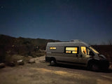 Experience van life with this RV rental! A cozy white camper van under a starry night sky, nestled against dark mountains.