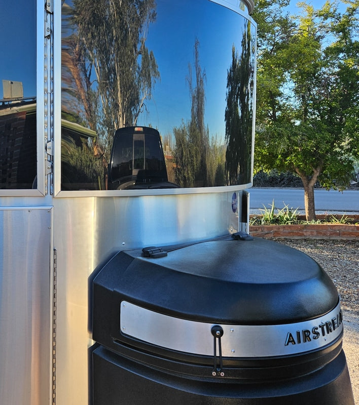 Front of a polished Airstream RV rental, reflecting blue sky and trees. Its silver body contrasts with a black tank cover. — photo 6