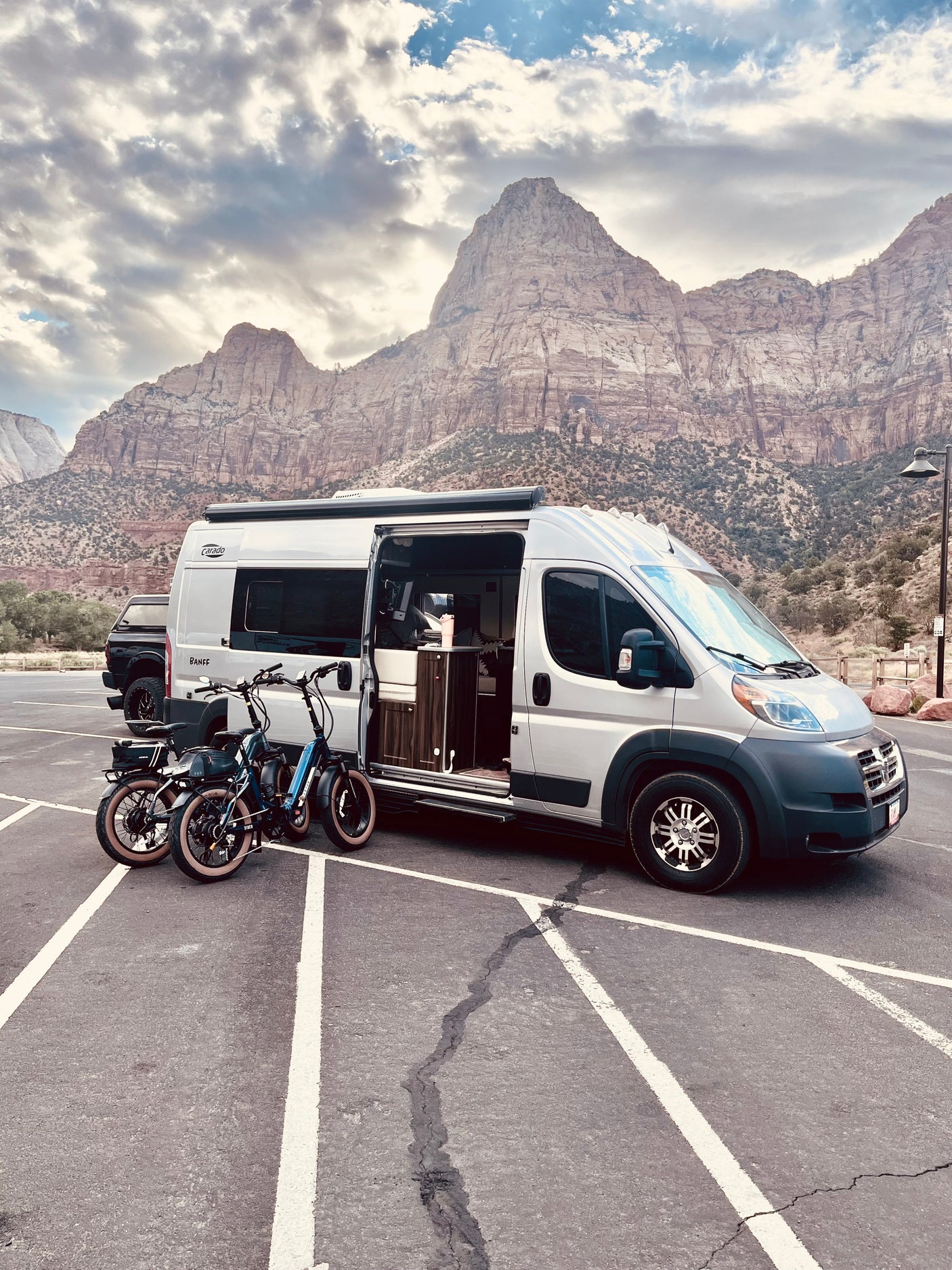 Grey RV rental parked with electric bikes, majestic mountains in background. Ready for a national park adventure!