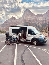 Grey RV rental parked with electric bikes, majestic mountains in background. Ready for a national park adventure!