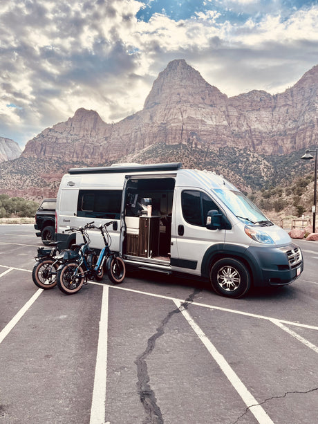 Grey RV rental parked with electric bikes, majestic mountains in background. Ready for a national park adventure!